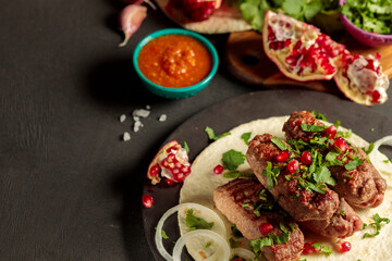 Kebab. Oblong cutlet of beef or lamb, served with vegetables, herbs, onions and pomegranate seeds on a thin pit with hot sauce.
