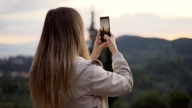 Blonde woman takes a photo of mountains with a smartphone in her hands