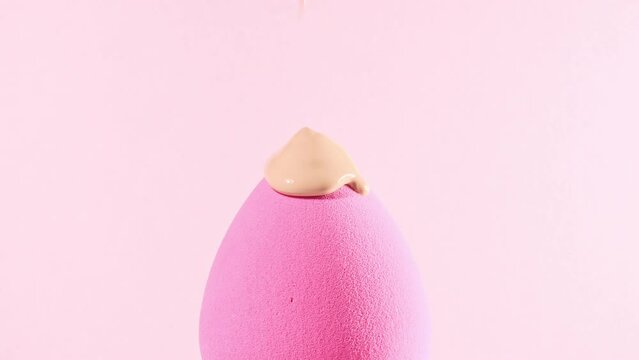 Make-up liquid beige foundation pouring on sponge, closeup. Cosmetic Dripping bb Cream on makeup brush on pink background. Macro Shot. Beautiful Makeup concept. High quality 4k footage