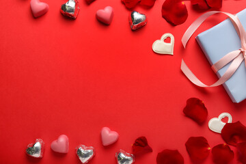 Composition with tasty heart-shaped candies and rose petals for Valentine's Day celebration on red background