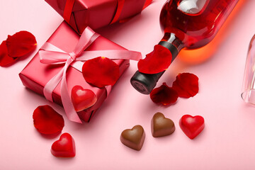 Composition with tasty heart-shaped candies and bottle of wine for Valentine's Day celebration on pink background, closeup
