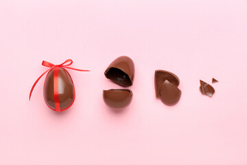 Composition with broken chocolate Easter eggs on pink background