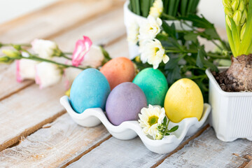 Easter composition, holiday home decor. Colourful eggs, flowers on the white wooden table. Copy space for text