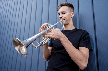 Young street musician playing the trumpet near the big blue wall