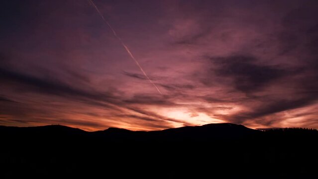 Beautiful clouded sunset sky timelapse with contrails from an airplane glowing through the clouds.