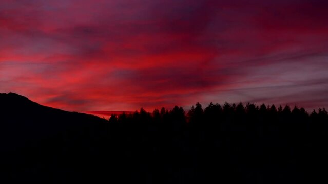 Stunning panning shot over the silhouette of forest and mountains against a gorgeous red purple sunset sky.