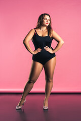 Sexy plus size fashion model in black one-piece swimsuit, fat woman in lingerie on pink background