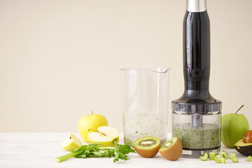 Black plastic electrical hand blender and accessories with sliced fruit on wooden background, space for text.