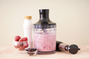 Hand blender for mixing organic fresh fruits smoothie on color background, healthy food.