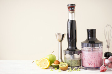 Black plastic electrical hand blender and accessories with fruit on wooden background, space for text. Flat lay.