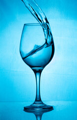 A glass of wine, a splash of wine-blue water on a blue background. A glass with a splash of wine on the blue background. Glass on the bar in a cafe, restaurant, nightclub or disco