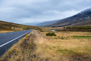 Highway road and mountain view during auto trip in Iceland. Spectacular Icelandic landscape with  scenic nature: fjords, fields, clouds, glaciers, waterfalls.