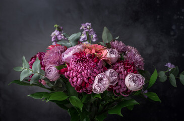 Beautiful bouquet of pink and purple flowers with green decorative leaves. Floral composition on black background.