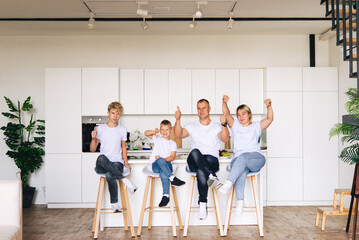 Cheerful family at home. Mom, dad and two sons. They eat cakes. Faces in cream. They sit on chairs in the kitchen. Celebration - Birthday, mother's day, father's day.