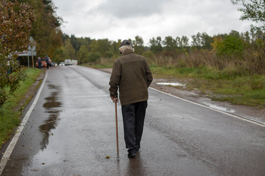 Old man walks down road. Pensioner with stick for support. Man with leg injury.