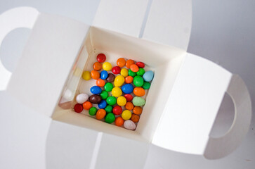 Small, multi-colored candies in a box, on a white background