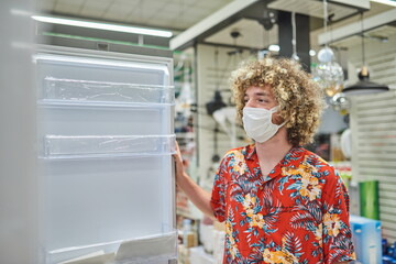 Shopping Concept. A Guy With Face Mask Buying Fridge In Supermarket.