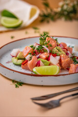 Salmon ceviche with avocado, onion, radish and lime on white plate and on beige background. Peruvian food. Delicious ceviche with salmon.