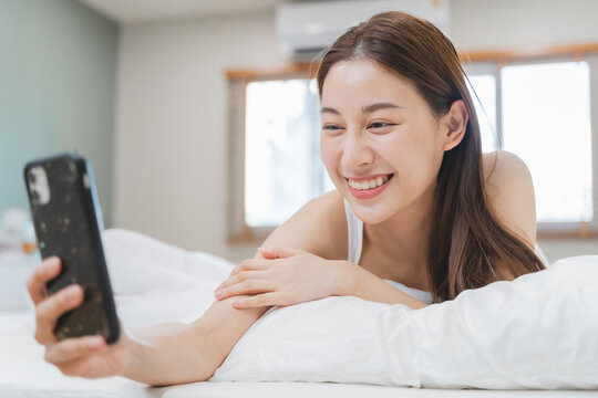 Happy Asian woman conference call via smartphone with her friends on the bed at home