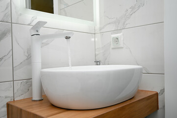 Naklejka na ściany i meble Modern bathroom sink in light colors with wood elements.