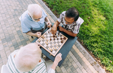 Group of senior friends playing chess at the park. Old multiethnic friends making activities outdoor. Concept about third age and lifestyle