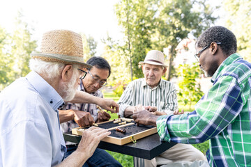 Group of senior friends playing chess at the park. Old multiethnic friends making activities...