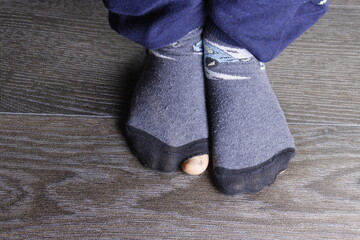 Worn out socks with a hole and toes sticking out of them on wooden floor.