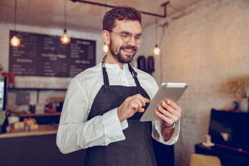 Cheerful male barista using tablet computer in cafe
