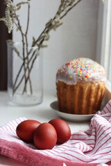Easter eggs on a cotton napkin and Easter cake in the background. Eggs dyed with natural onions on a rustic white window background. Natural ecological coloring with food coloring. View from above.