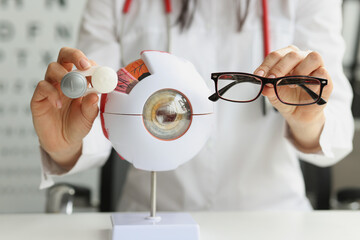 Optometrist woman holding glasses near anatomical model eye