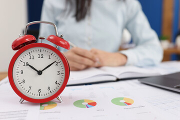 Red alarm clock on documents in the office, woman is blurry