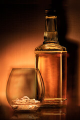 a bottle of rum , golden whiskey or liqueur . a glass of bourbon has a beautiful dark background....