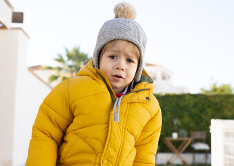 Cute and happy little boy in winter clothing having fun at the park on a sunny day. Beautiful blonde hair male toddler playing outdoors