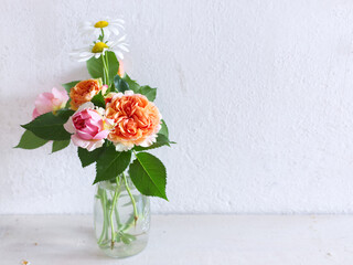 Spring flowers in a glass vase on a wooden table. Blurred kitchen background. Bouquet of roses and Leucanthemum. Contemporary elegant scandi interior.
