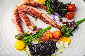 Octopus with black risotto. Carrot cream, mini-broccoli, basil pesto. Delicious healthy traditional food closeup served for lunch in modern gourmet cuisine restaurant