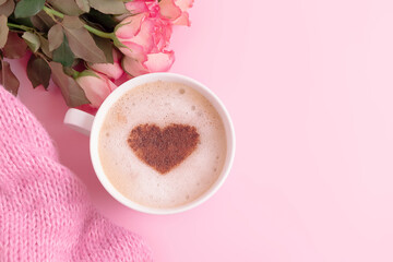 Obraz na płótnie Canvas Romantic composition with coffee cup with heart on top, flowers and knitted blanket on pastel pink background and copy space