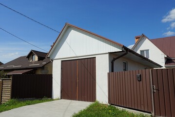 facade of a white garage with brown gates and part of a metal fence wall on the street against a blue sky