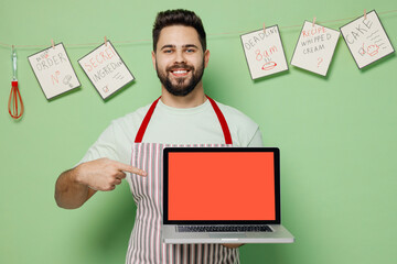 Young male chef confectioner baker man in striped apron hold use work point on laptop pc computer with blank screen workspace area isolated on plain pastel light green background Cooking food concept.