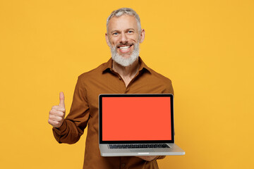 Happy elderly gray-haired bearded man 40s years old wears brown shirt hold use point finger on laptop pc computer with blank screen workspace area isolated on plain yellow background studio portrait.