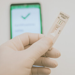 Closeup view of gloved hand with SARS-CoV-2 rapid antigen test nasal and phone with green digital...