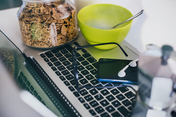 Table set for breakfast, kitchen in the background. Natural meal and technology devices. Interior view of a cozy and modern home. Millennial, youth, home working, home schooling, remote work concept.