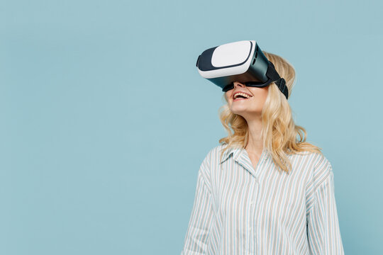 Elderly amazed happy caucasian woman 50s wearing casual striped shirt watching in vr headset pc gadget isolated on plain pastel light blue color background studio portrait. People lifestyle concept. - Powered by Adobe
