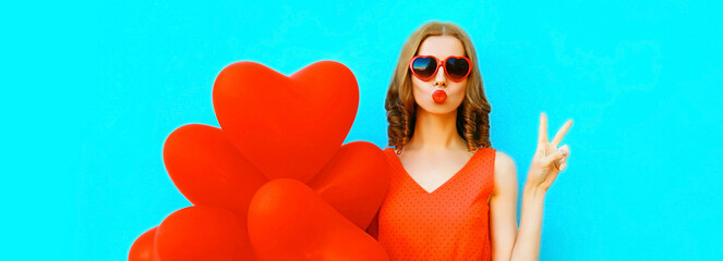 Portrait of beautiful young woman with red heart shaped balloon blowing her lips sending sweet air...