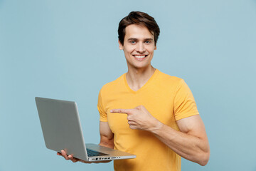 Young smiling happy satisfied man 20s in yellow t-shirt hold use work point index finger on laptop...