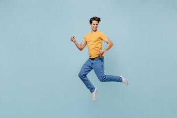 Fototapeta premium Full body musician happy caucasian brunette young man 20s wearing yellow t-shirt jump high play guitar isolated on plain pastel light blue color background studio portrait. People lifestyle concept.