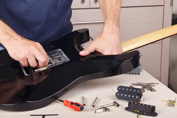 Guitar technician adjusts springs of tremolo bridge on modern electric guitar.