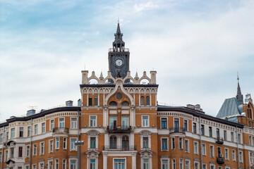 Fototapeta premium The facade of an old brown architectural building with a clock on the tower against a blue sky background