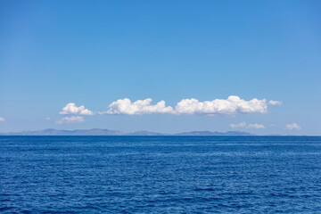 Obraz premium Rippled Aegean Sea, cloud on blue sky over Serifos island rocky land. Seascape, Cyclades Greece.