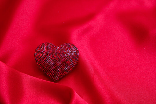 Red color ruby heart jewel on empty silk background. Valentine day, love celebration.