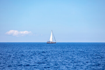 Sailing boat with open white sail, blue sky and rippled sea background